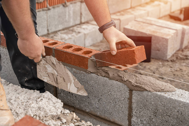 Bricklayer laying brick on cement mix on construction site close-up. Reduce the housing crisis by building more affordable houses concept - Photo, Image