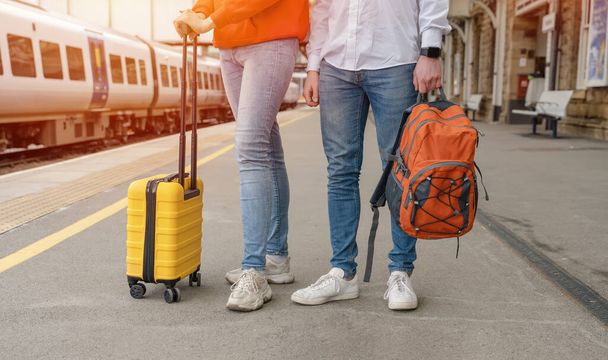 Путешественники с рюкзаком и желтым чемоданом ждут поезда на вокзале. Пара опоздала на поезд. Концепция путешествия. - Фото, изображение