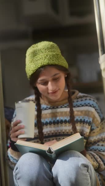 Hippi yaşam tarzını tamamen benimseyen şık genç bir bayan, bahçede bir kitap ve sıcak bir içecekten hoşlanıyor. Yüksek kalite 4k görüntü - Video, Çekim