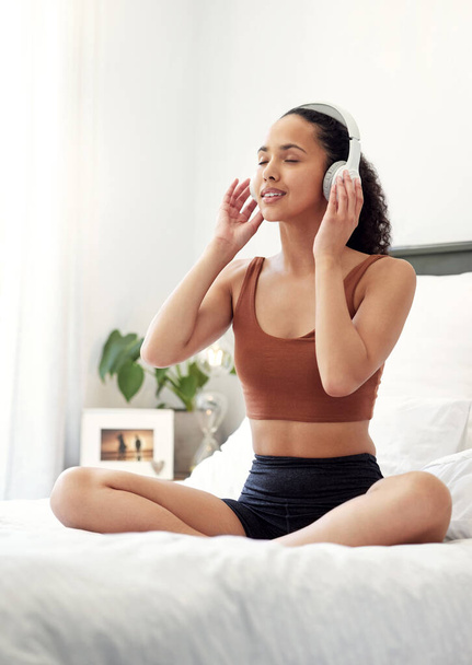 Belélegezni a jóságot, kilélegezni a negativitást. egy fiatal nő zenét hallgat, miközben otthon ül az ágyán. - Fotó, kép