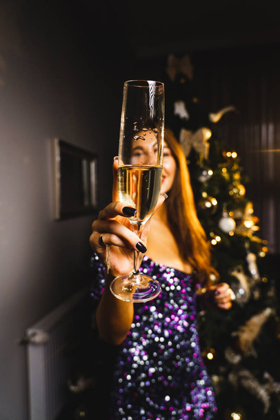 Una donna carina posa con un bicchiere di champagne vicino all'albero di Natale. Il concetto di Capodanno e le vacanze di Natale - Foto, immagini
