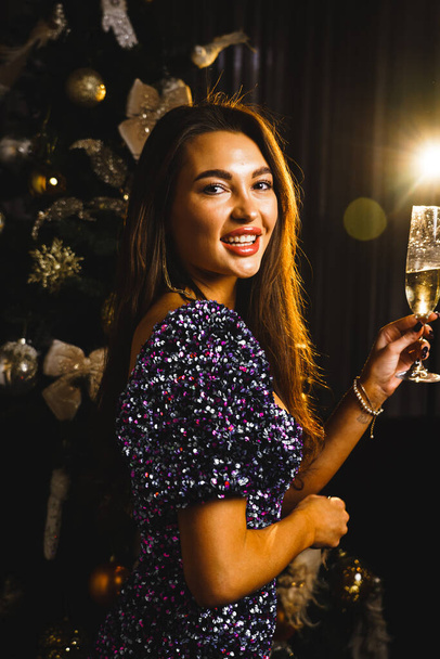 Une jolie femme pose avec une coupe de champagne près du sapin de Noël. Le concept du Nouvel An et des vacances de Noël - Photo, image