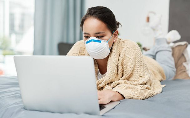 Проверяю обновления и последние новости о вирусе. женщина в маске, лежа на кровати с ноутбуком - Фото, изображение