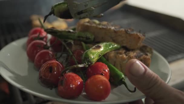 A séf átviszi a sült halat, paradicsomot és zöldséget a grillből egy tányérra. Lassú mozgás, közelkép. - Felvétel, videó