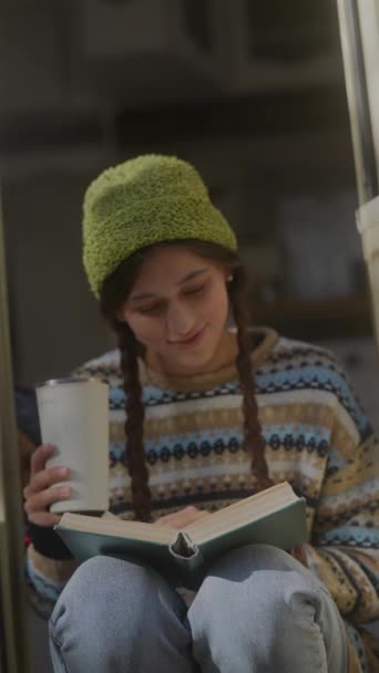 Avec son ambiance hipster, une belle fille savoure un livre et une boisson chaude dans le jardin d'automne. Images 4k de haute qualité - Séquence, vidéo