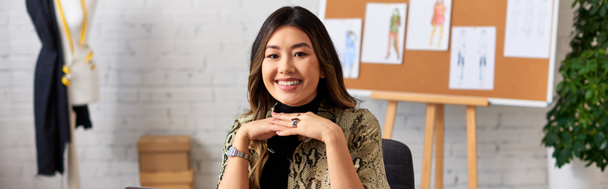 fröhliche und modische asiatische Kleidungsdesignerin blickt in privates Atelier, Banner - Foto, Bild