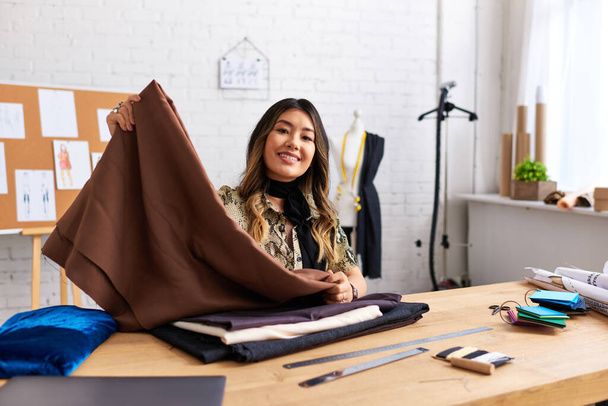 nadšený asijský designér s kvalitním vzorkem textilie při pohledu na kameru v moderním osobním ateliéru - Fotografie, Obrázek