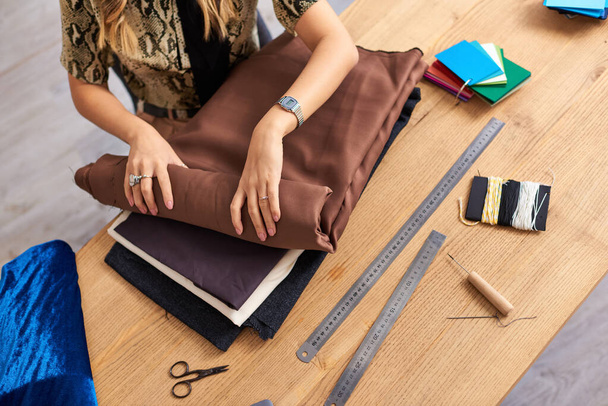 vista cortada de roupas estilista verificando amostras de tecidos perto de suprimentos de costura no atelier de moda - Foto, Imagem