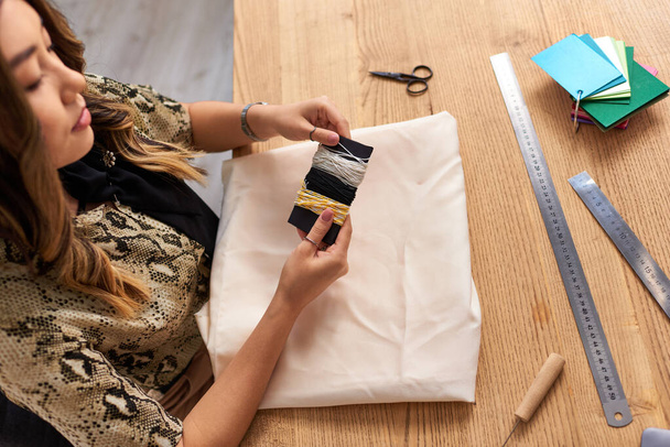 alto ângulo vista de asiático estilista com fios perto de tecido e costura suprimentos no estúdio de moda - Foto, Imagem