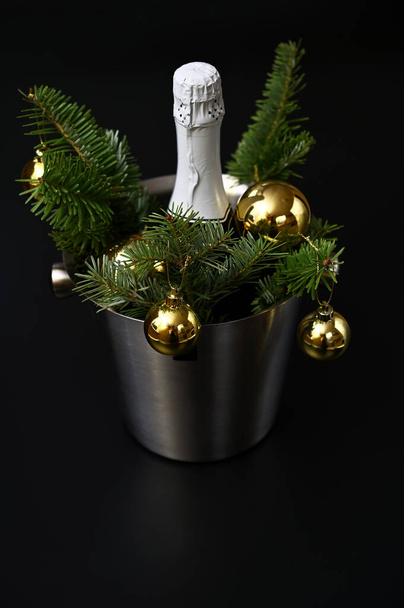 Πρωτοχρονιάτικη διακόσμηση, ένα μπουκάλι σαμπάνια, κλαδιά ελάτης και χρυσές μπάλες σε σκούρο φόντο - Φωτογραφία, εικόνα