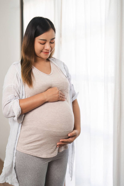 Retrato de una hermosa joven durante el tercer trimestre del embarazo Mujer embarazada con brazos en el vientre redondo, sonriente, expresión relajada.. - Foto, imagen