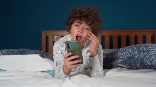 Ragazzo di 9 anni felice di stare in camera da letto guardando lo smartphone - dipendenza dai social network e da Internet - trascorrendo troppo tempo online durante la vita quotidiana - Filmati, video