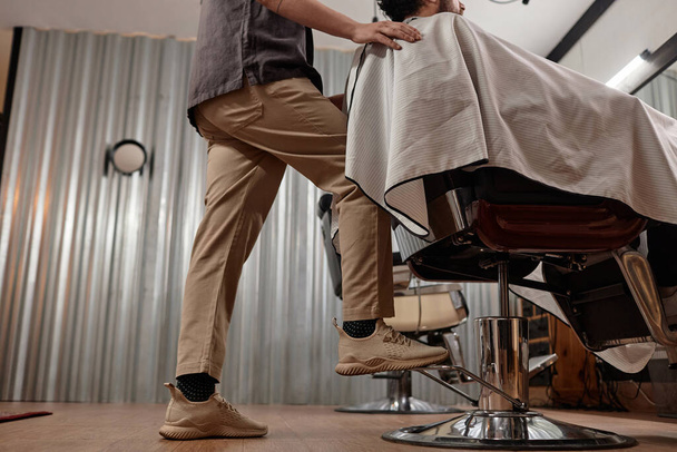 Низкий угол зрения парикмахерского кресла с клиентом и подготовка к стрижке - Фото, изображение