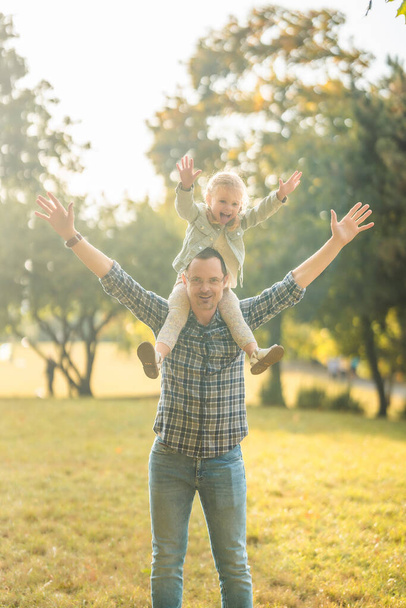 Молодой отец и симпатичная маленькая девочка веселятся вместе в осеннем парке при закатном свете Европы. Высокое качество фото - Фото, изображение