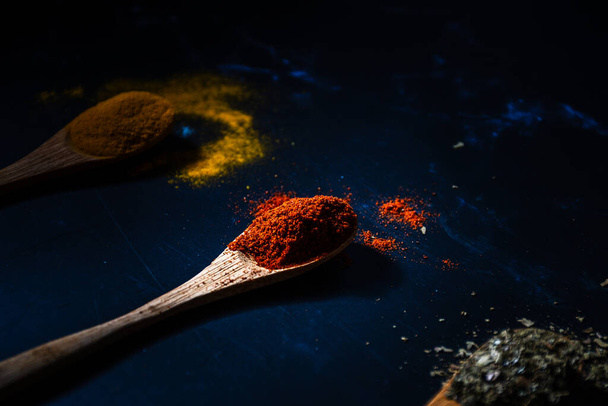 Wooden spoons with turmeric and red pepper on a dark background. - Photo, Image