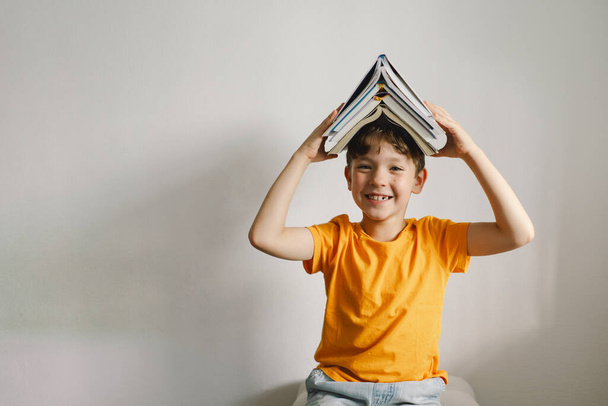 Een leuke jongen met een oranje T-shirt zit op een zachte poef een boek te lezen. Begrepen, ruimte. Echte mensen en levensstijl - Foto, afbeelding