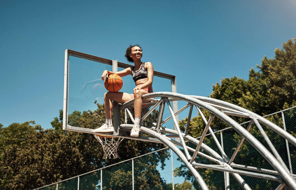 Haben Sie das Zeug, der Beste zu werden? eine sportliche junge Frau sitzt auf einem Basketballkorb auf einem Sportplatz - Foto, Bild