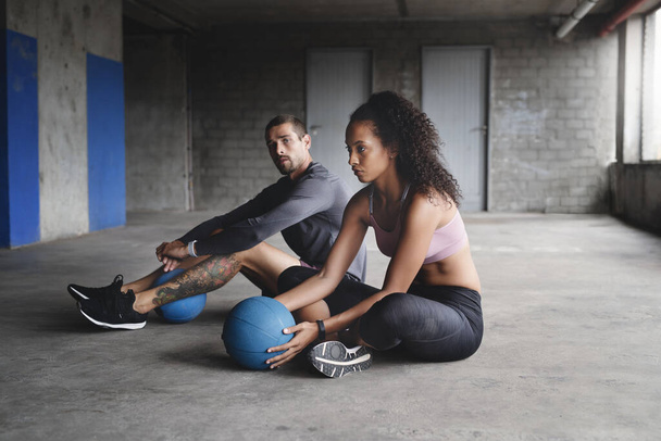Запускаем шар. Полнометражный снимок спортивной молодой пары, сидящей и упражняющейся с мячом на парковке - Фото, изображение