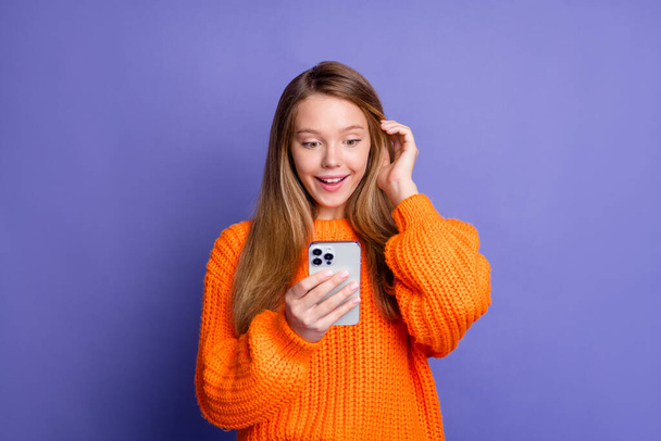 Photo de mignonne jeune fille toucher ses cheveux navigation smartphone excité passer du temps sur Internet isolé sur fond de couleur violette. - Photo, image