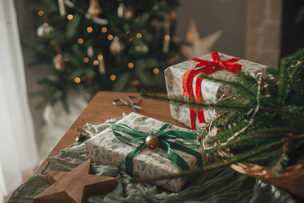 Veselé Vánoce a veselé svátky! Stylové zabalené vánoční dárky, rustikální koš s jedlovými větvemi a moderní dekorace na stole zblízka. Atmosférický skandinávský obraz - Fotografie, Obrázek