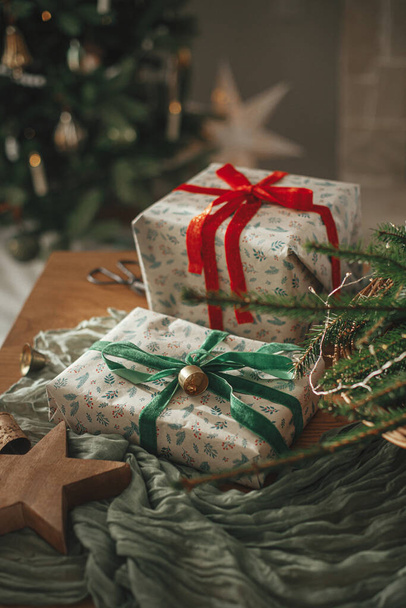 Joyeux Noël et Joyeuses fêtes ! Cadeaux de Noël élégants enveloppés, panier rustique avec branches de sapin et décorations modernes sur la table close up. Image scandinave atmosphérique - Photo, image