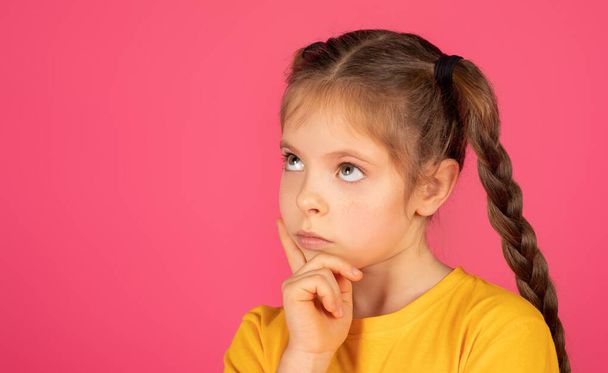 Let me think. Doubtful preteen girl looking aside at copy space, thoughtful female child dreaming, imagining something, creating idea while posing isolated over pink studio background, closeup - Photo, Image