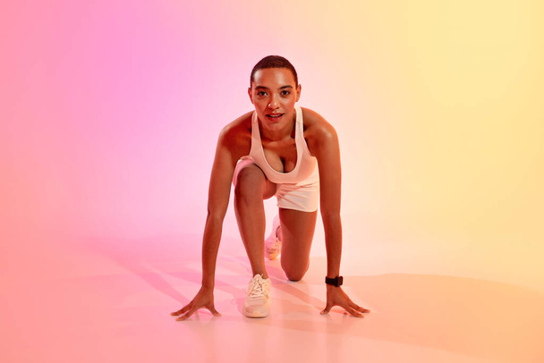 Pozytywna młoda Latynoska atletka w odzieży sportowej stoi na starcie, gotowa do biegu na neonowym różowym tle studia. Bieganie, sport zawodowy, opieka zdrowotna, odchudzanie i dopasowanie - Zdjęcie, obraz