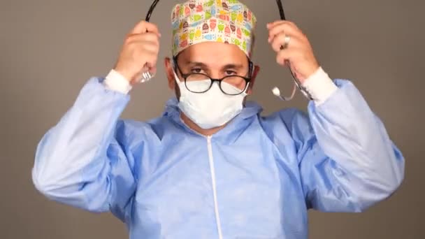 Γιατρός με μάσκα και χειρουργικά ρούχα φορώντας ένα στηθοσκόπιο - Πλάνα, βίντεο