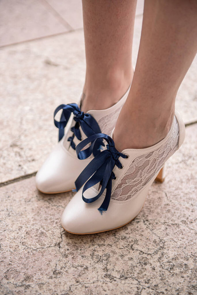 Mavi bağcıklı ve dantelli beyaz kadın ayakkabıları, bir kadının ayağında. - Fotoğraf, Görsel