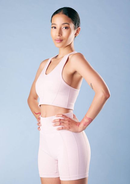 Mixed race fitness woman standing with her hands on her hips in studio against a blue background. Beautiful young hispanic female athlete exercising or working out. Dedicated to health and fitness. - Photo, Image