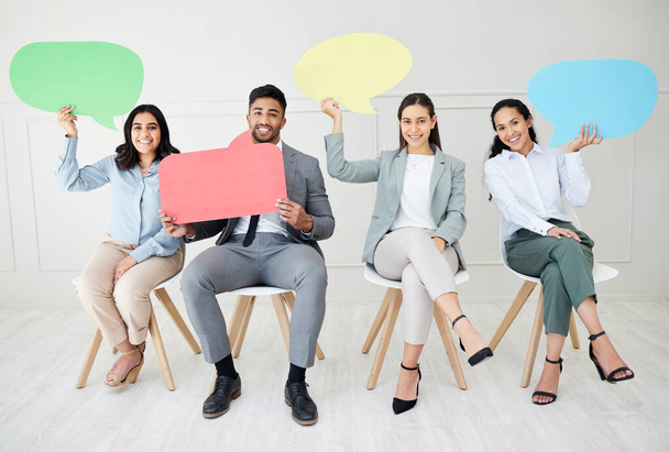 Say it again for the people in the back. Portrait of a group of businesspeople holding speech bubbles while sitting in line against a grey background - Photo, Image