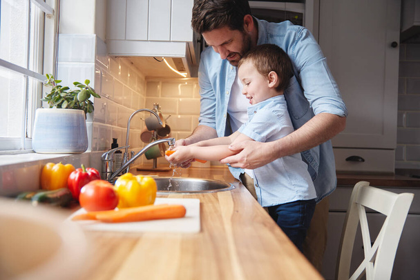 El primer paso para preparar una comida. un niño y su padre enjuagando verduras en casa - Foto, Imagen