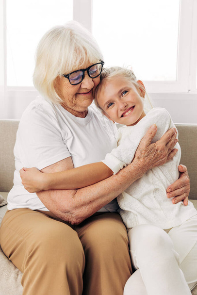 Sitting woman granddaughter generation old hug happy love lifestyle bonding daughter child home couch mother grandmother elderly sofa hugging senior family girl - Photo, Image