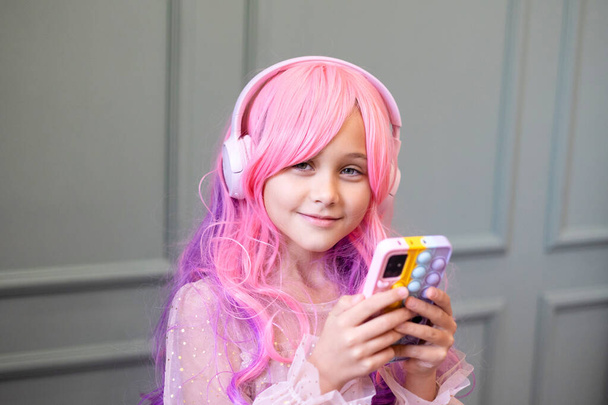 Βανίλια. Kawaii δονήσεις. Το κοριτσάκι με τα ροζ μαλλιά κάνει πάρτι σε στυλ Μπάρμπι. Ακρόαση μουσικής με ακουστικά, κινητό τηλέφωνο. - Φωτογραφία, εικόνα