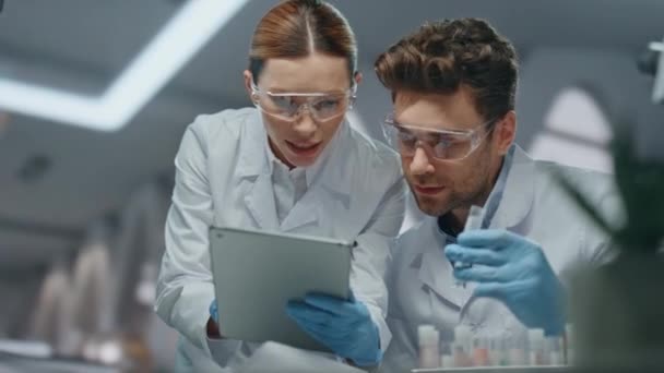 Lab colleagues researching cure virus disease in advanced clinic closeup. Woman doctor with tablet discussing experiment data with man biochemist. Two scientists in glasses analyzing medical expertise - Footage, Video