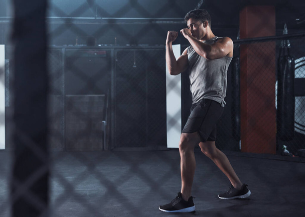 Бийся за фітнес, який ти заслуговуєш. молодий чоловік практикує свою рутину кікбоксингу в спортзалі - Фото, зображення