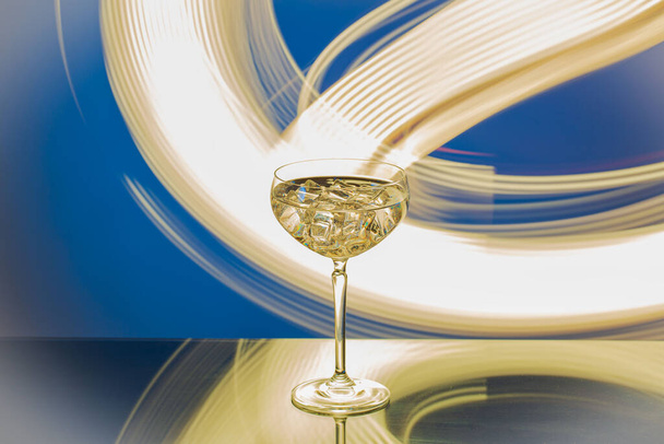 Piękny widok ze szklanki martini z lodem na abstrakcyjnym tle żółto-biało-niebieskim. - Zdjęcie, obraz