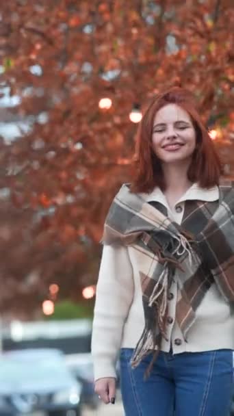 Ubrana w jesienny strój, rudowłosa dziewczyna wędruje po ulicach miasta. Wysokiej jakości materiał 4k - Materiał filmowy, wideo