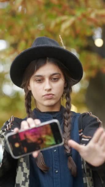 Le strade della città autunnali presentano una ragazza alla moda che prende selfie in un insieme di cappelli e hippie. Filmati 4k di alta qualità - Filmati, video