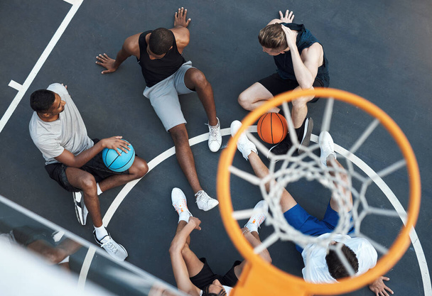 スポーツはコミュニティをまとめる上で重要な役割を果たしています. バスケットボールコートにぶら下がっているスポーティな若者のグループの高角度ショット - 写真・画像