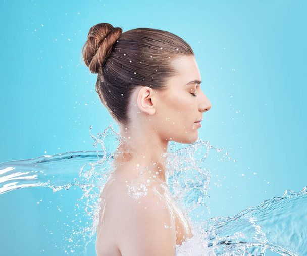 Es ist erstaunlich, was eine Dusche bewirkt. eine schöne junge Frau wird vor blauem Hintergrund mit Wasser bespritzt - Foto, Bild