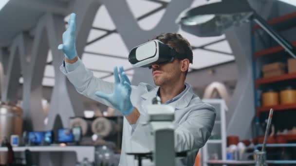İleri düzey laboratuvarda fütüristik simülasyonla çalışan VR gözlüklü kimyager. Ciddi bir bilim adamı bilimsel araştırmalar için sanal gerçeklik kulaklığı kullanıyor. Laboratuar biyomühendisleri arayüze dokunuyor. - Video, Çekim