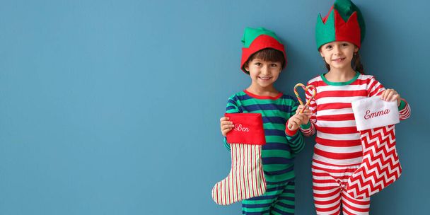 Cute little children in pajamas and with Christmas socks on blue background with space for text - Photo, Image
