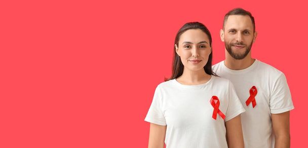 Junges Paar mit Bewusstseinsbändern auf rotem Hintergrund mit Platz für Text. Banner zum Welt-AIDS-Tag - Foto, Bild