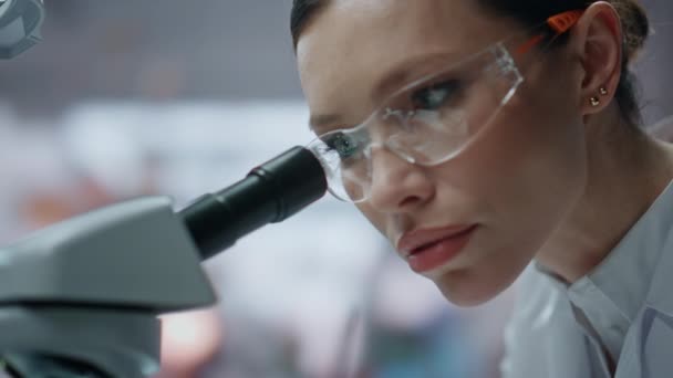 Closeup βιοχημικός αναζητούν μικροσκόπιο διερεύνηση δείγμα στο εργαστήριο κλινική. Προσωπογραφία νεαρής γυναίκας επιστήμονα που εξετάζει την προετοιμασία στο εργαστήριο. Επαγγελματική γυναίκα ειδικός που κάνει βιοχημική έρευνα - Πλάνα, βίντεο