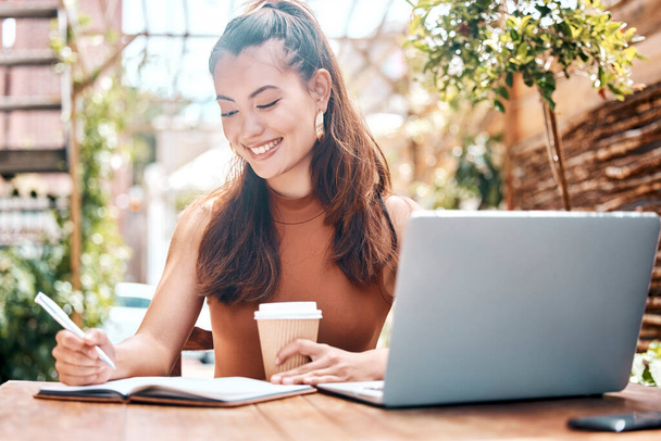 Freelance entrepreneur working in a restaurant, planning, writing notes in her notebook. Smiling young businesswoman drinking coffee, working on her laptop in a cafe. Teleworking businesswoman in caf. - Photo, Image