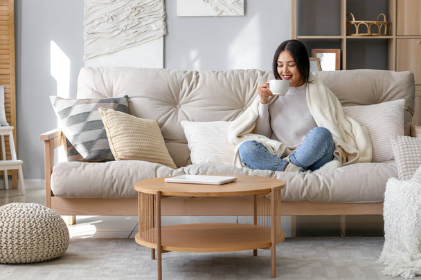Joven asiática mujer con caliente a cuadros beber té en casa - Foto, Imagen