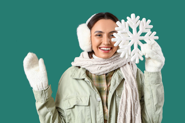 Young woman in winter clothes with snowflake on green background - Photo, Image