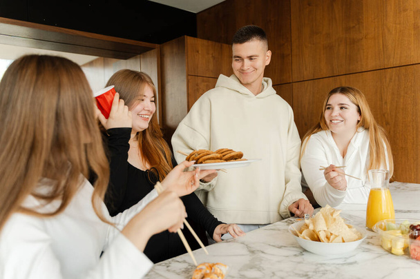 Друзі збираються за обіднім столом з соком і закусками. Щасливі молоді люди їдять, святкують свято, розмовляють, розслабляються разом у вихідні - Фото, зображення