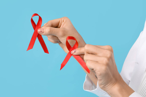 Female doctor with red ribbons on blue background, closeup. World AIDS Day concept - Photo, Image